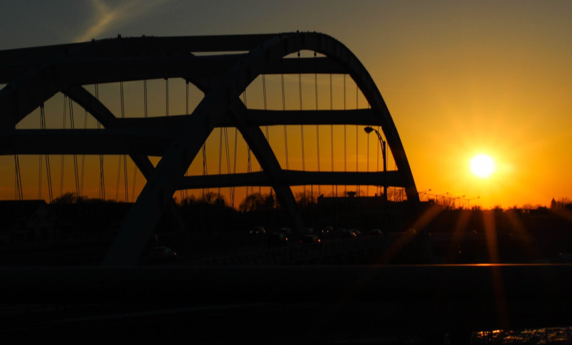 a golden yellow sunset just over the horizon and the hints of cars traveling along the arching silhouette of a bridge.